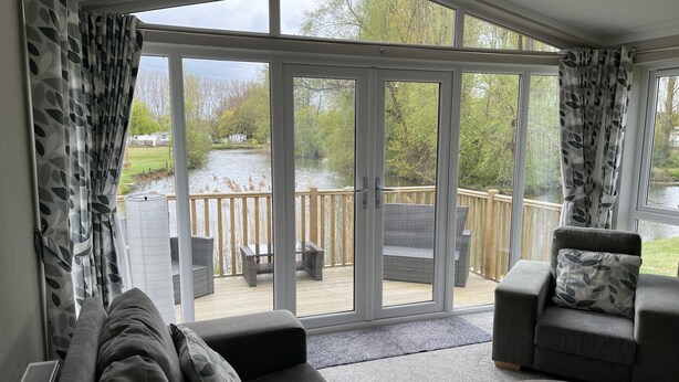 A modern living room with a large sliding glass door leading to a deck overlooking a lake. - Beautiful and Tranquil Lakeside Lodge - Sleeps 5 (Northampton)