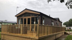 A wooden decked structure with a covered area, likely a cabin or small house, surrounded by grass and other similar structures. - Beautiful and Tranquil Lakeside Lodge - Sleeps 5 (Northampton)