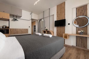 A modern hotel room with a large bed, wooden paneling, a flat-screen TV, a round mirror, and a small shelf with a plant.