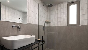 A modern bathroom with a large white sink, a glass shower enclosure, and a window. - Santa Maria City Hotel (Rhodes)