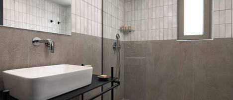 A modern bathroom with a large white sink, a glass shower enclosure, and a window.