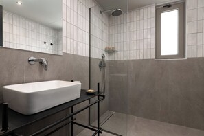 A modern bathroom with a large white sink, a glass shower enclosure, and a window. - Santa Maria City Hotel (Rhodes)