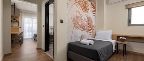 A bedroom with a bed, a small bedside table, a wall-mounted air conditioner, and a window.