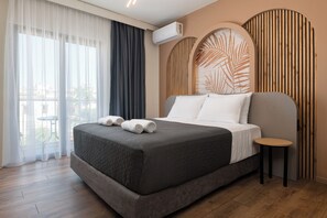 A hotel room with a bed, a small table, an air conditioning unit, and a view through the window. - Santa Maria City Hotel (Rhodes)