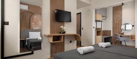 A modern hotel room with a large bed, a TV, a desk with a chair, and a mirror.