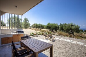 Un patio al aire libre con mesa y sillas de madera, una parrilla incorporada y vistas del paisaje circundante.