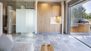 Une cuisine moderne avec des meubles en bois et une cloison en verre, un coin repas avec un canapé à motifs et une vue à travers une porte coulissante.