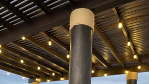 Ulkoterassi, jossa on puinen pöytä ja tuolit, pergola, jossa on valonauhat, ja näkymä kaupunkimaisemaan.