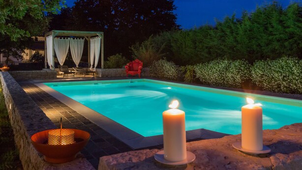 A swimming pool with a gazebo, two candles, and a red chair.