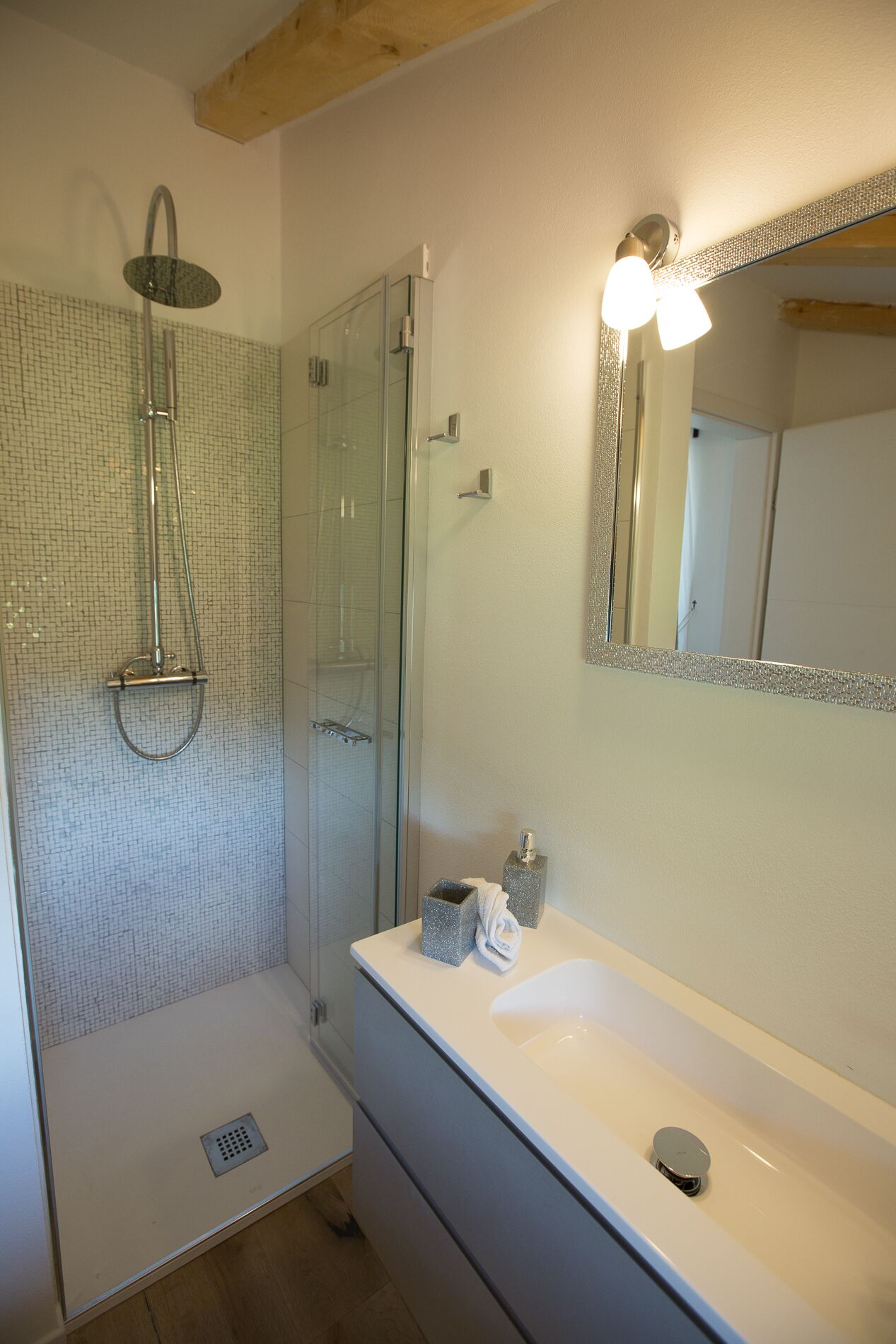 A modern bathroom with a glass shower enclosure, a white sink, and a mirror with a decorative frame.