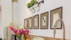 A modern kitchen with a stainless steel sink, a fruit bowl, and a decorative wall with framed botanical prints.