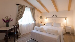 A bedroom with a bed, bedside tables, a desk, a chair, a potted plant, and a window with curtains.