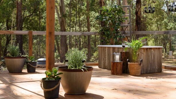 An outdoor patio area with wooden flooring, potted plants, and a wooden fence. - The Love Shack (Wheatsheaf)