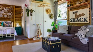 A cozy living room with a wooden floor, a brown sofa, a white table, and a suitcase labeled "FootJoy." - The Love Shack (Wheatsheaf)