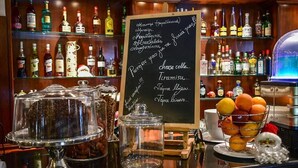 Zona de bar con una pizarra mostrando un menú de bebidas y postres, estantes con botellas de licor y un frutero en la barra.