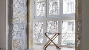 Um quarto com uma janela grande, uma cama e uma cadeira de madeira.