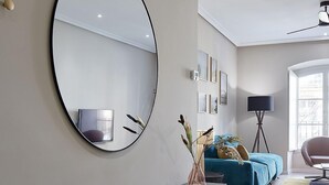 Uma sala de estar moderna com um espelho redondo grande, um console preto, um sofá azul e um abajur de chão.