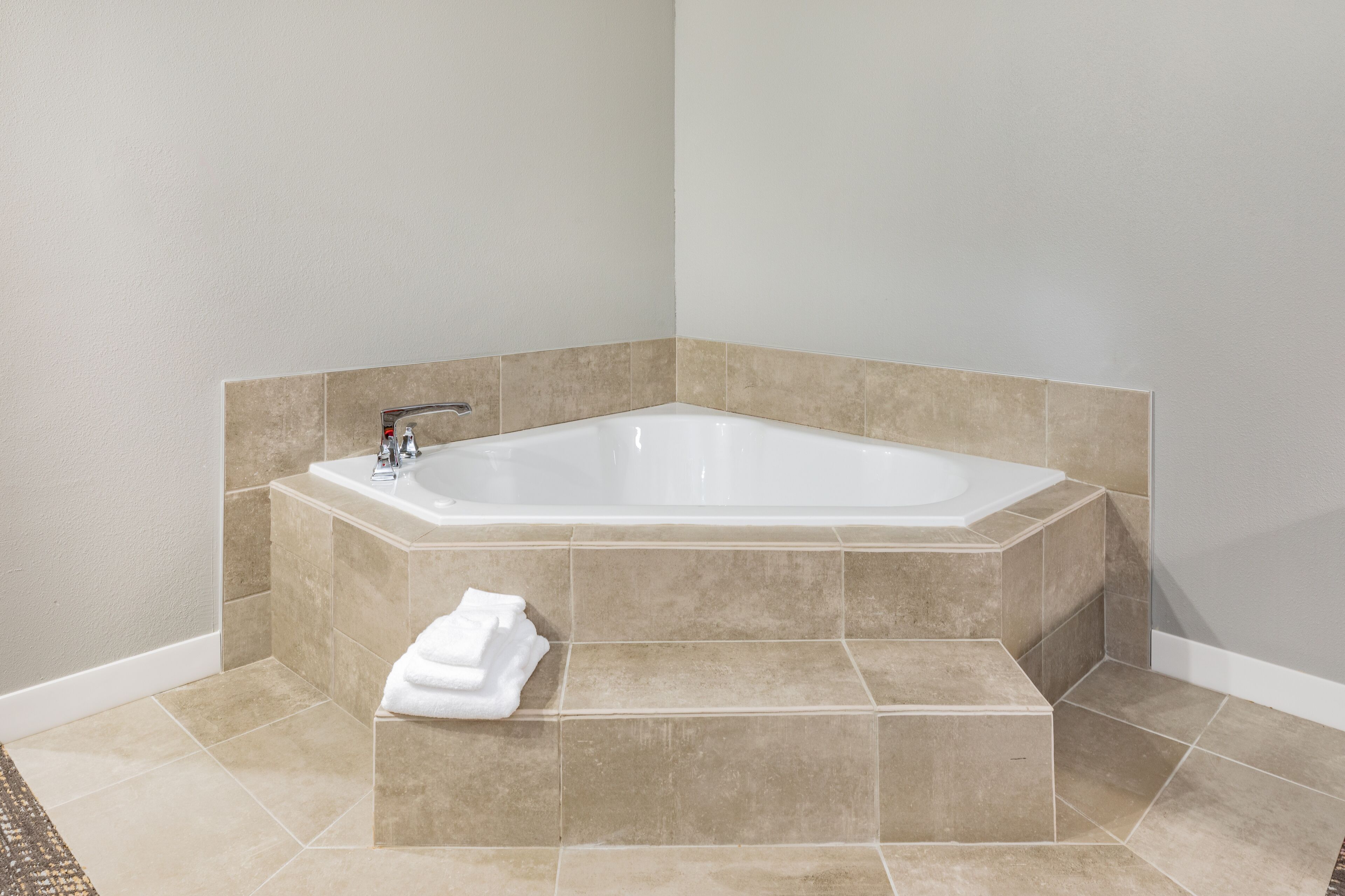A corner bathtub with beige tiles, a white towel, and a white wall.