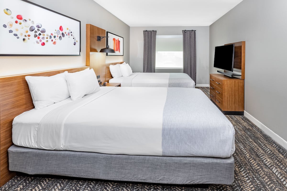 Quarto de hotel com duas camas, televisão, escrivaninha e janela com cortinas.