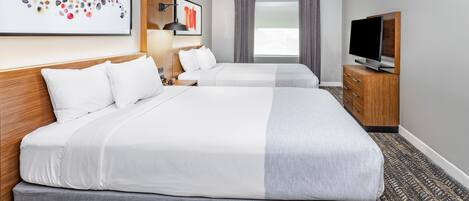 Una habitación de hotel con dos camas, televisión, escritorio y ventana con cortinas.