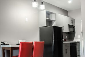 A modern kitchen with white cabinets, a black refrigerator, and red chairs at a dining table. - Hawthorn Extended Stay by Wyndham Oklahoma City Airport (Oklahoma City)
