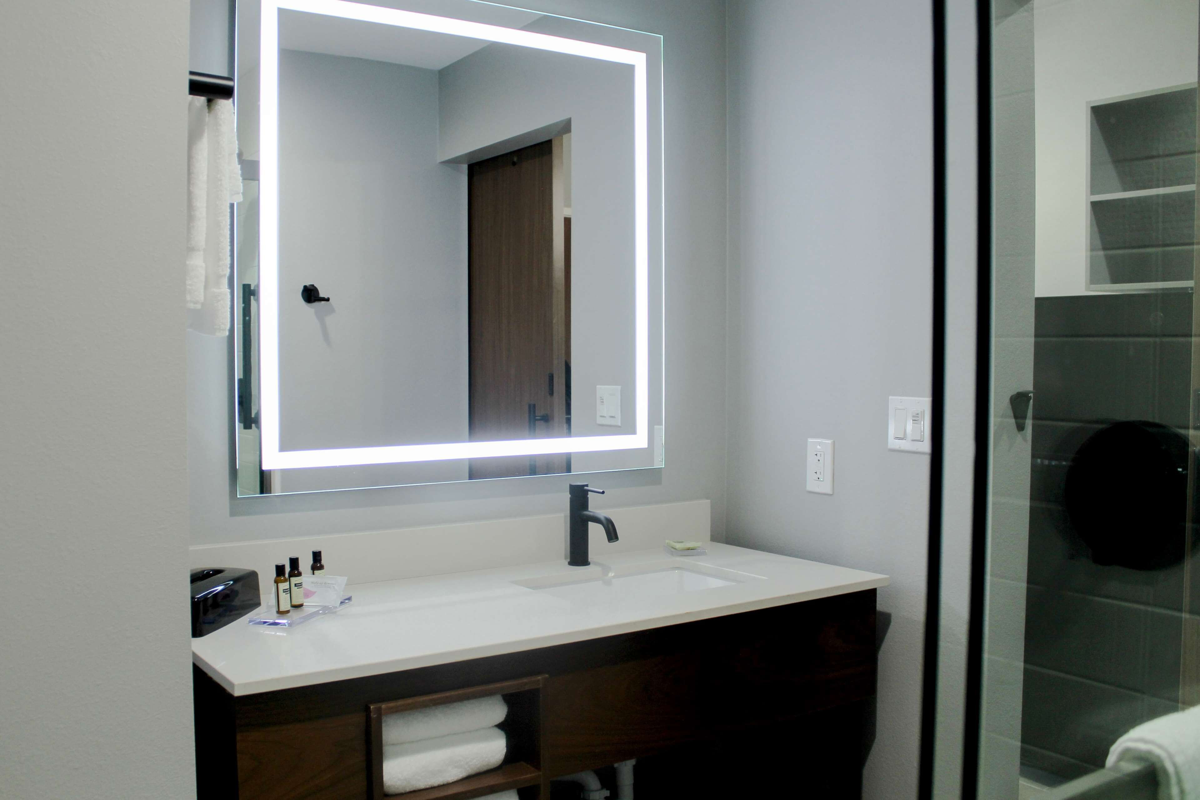 A modern bathroom with a large mirror, white sink, and a glass shower enclosure.