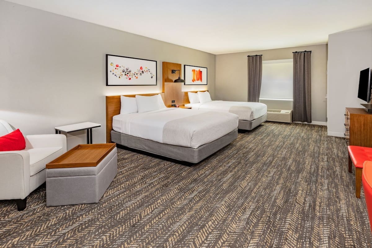 Quarto de hotel com cama, duas mesas de cabeceira, um sofá, uma mesinha e uma televisão.
