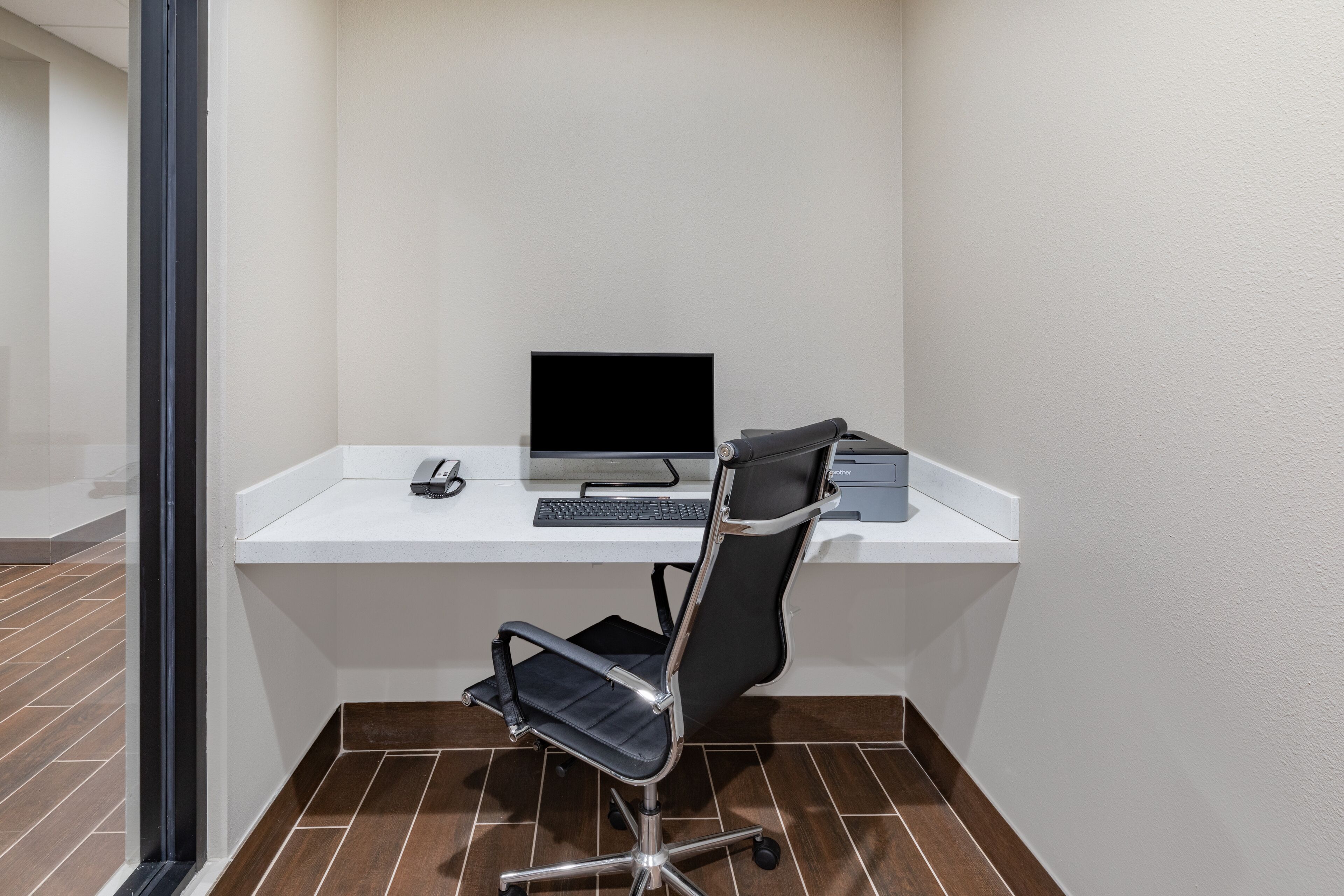 A modern office space with a white desk, a black office chair, a computer, and a telephone.