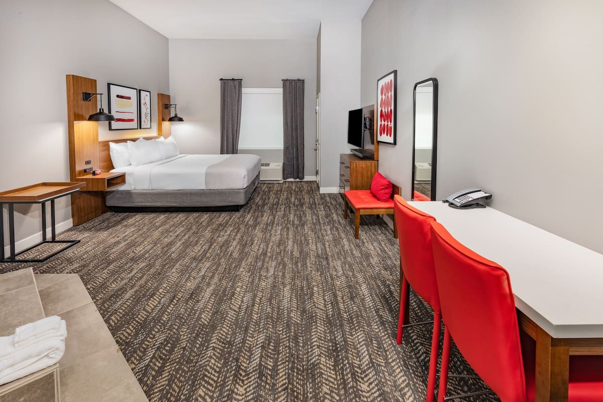 Quarto de hotel moderno com uma cama grande, uma escrivaninha, uma cadeira, uma televisão e um telefone.