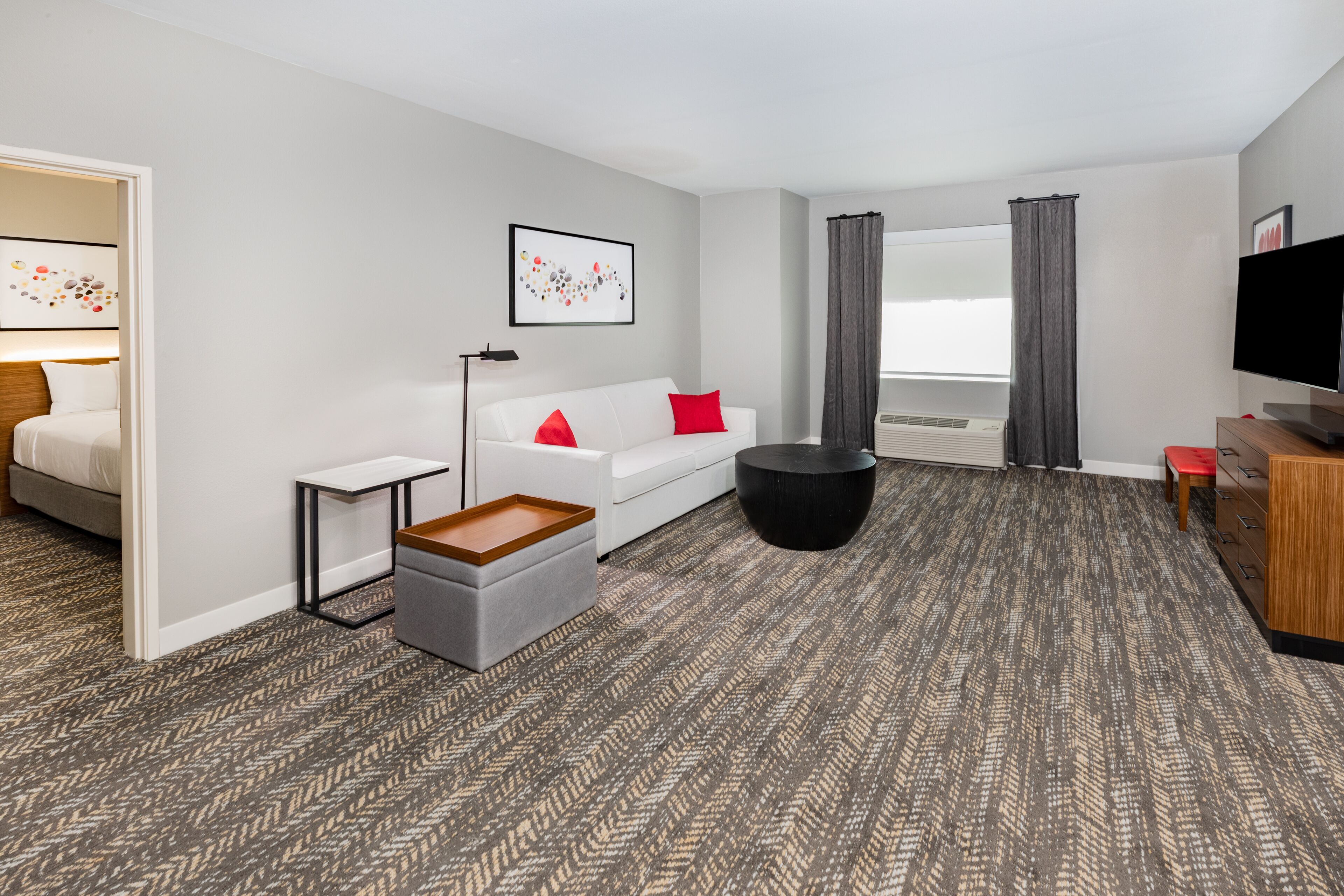 Ein modernes Hotelzimmer mit einer Couch, Hocker und einem Flachbildfernseher.