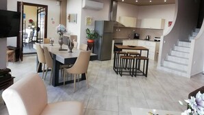A modern kitchen with a central island, a dining area with a table and chairs, and a staircase leading to an upper level. - Endless Blue/luxury Apartment (Kavala)