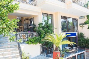 Edificio de dos plantas con balcón, mobiliario exterior y plantas en macetas.