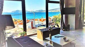 A spacious living room with large windows offering a view of the sea and buildings. - Endless Blue/luxury Apartment (Kavala)