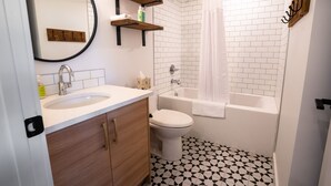 Een badkamer met een wastafel, toilet en bad. Boven de wastafel zijn houten planken en er hangt een spiegel aan de muur.