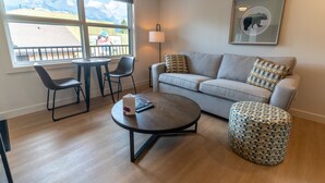 Een woonkamer met een bank, twee stoelen, een salontafel, een lamp en een raam met uitzicht op bergen.
