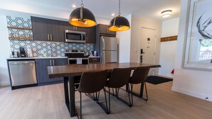 A modern kitchen with dark wood cabinets, stainless steel appliances, and a central island with chairs. - Basecamp Suites Canmore I Two Bedroom Apartment (Canmore)