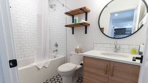A bathroom with a white bathtub, toilet, and sink, with a mirror above the sink and a shower curtain. - Basecamp Suites Canmore I Two Bedroom Apartment (Canmore)