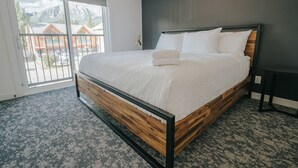 Ein modernes Schlafzimmer mit einem großen Bett, einem dunklen Kopfteil und Bergblick durch eine Schiebetür.