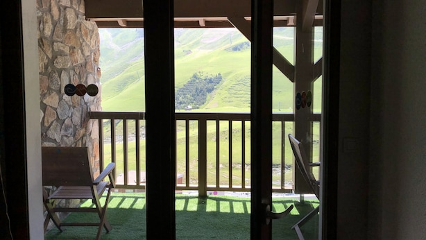 Een balkon met een stenen muur, een houten stoel en uitzicht op glooiende groene heuvels.