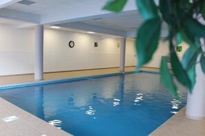 Una piscina interior con agua cristalina, suelo de baldosas y un reloj en la pared.