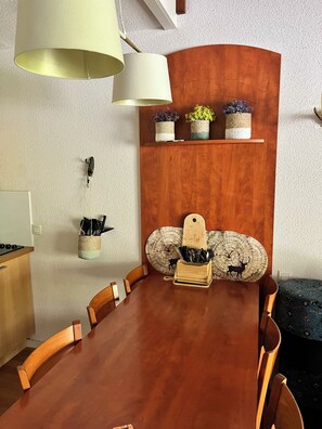 Un comedor con una mesa de madera, sillas, una lámpara colgante, un estante con plantas en macetas y un bloque de cuchillos fijado a la pared.