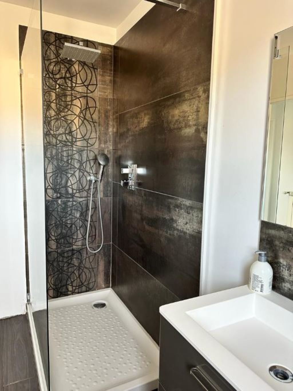 Un baño moderno con ducha, un lavabo blanco y un espejo grande.
