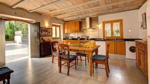 A spacious kitchen with wooden cabinets, a dining table with chairs, and a large window providing natural light. - Villa Llobiner, Perfect location! A country villa by Renthousing (Pollença)