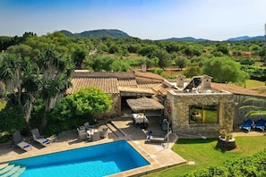 A poolside area with lounge chairs, a stone building with a glass window, and a view of the surrounding greenery and hills.