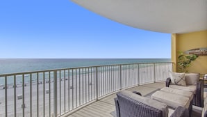 A balcony with a view of the beach, wicker furniture, and a sign reading "The Beach Happy Place". - Emerald Isle 504 - Front Row Beach chair service included! Affordable rates! (Panama City Beach)