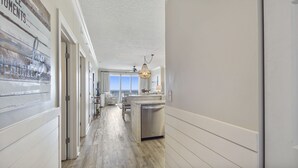 A spacious hallway with a view to the ocean, a dining area with a view, and a kitchen with a dishwasher. - Emerald Isle 504 - Front Row Beach chair service included! Affordable rates! (Panama City Beach)