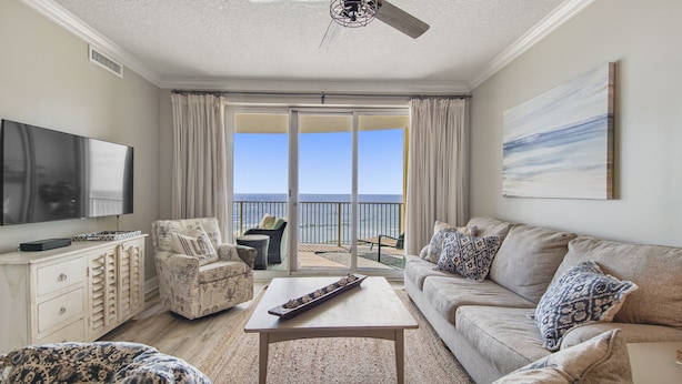 A living room with a TV, a sofa, a coffee table, and a balcony with a view of the sea. - Emerald Isle 504 - Front Row Beach chair service included! Affordable rates! (Panama City Beach)