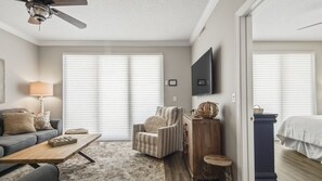 Un salon spacieux comprenant un canapé, un fauteuil, une table basse et un téléviseur fixé au mur.