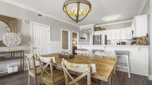 Une cuisine spacieuse avec des meubles blancs, une table à manger en bois et un lustre.