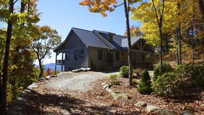 A cabin with a porch, surrounded by autumn foliage and a gravel path.